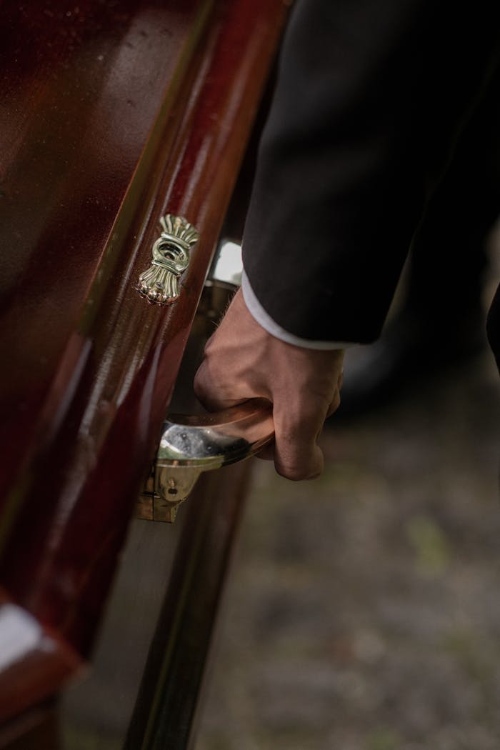 Close-up of a hand holding a wooden casket handle during a funeral ceremony.
